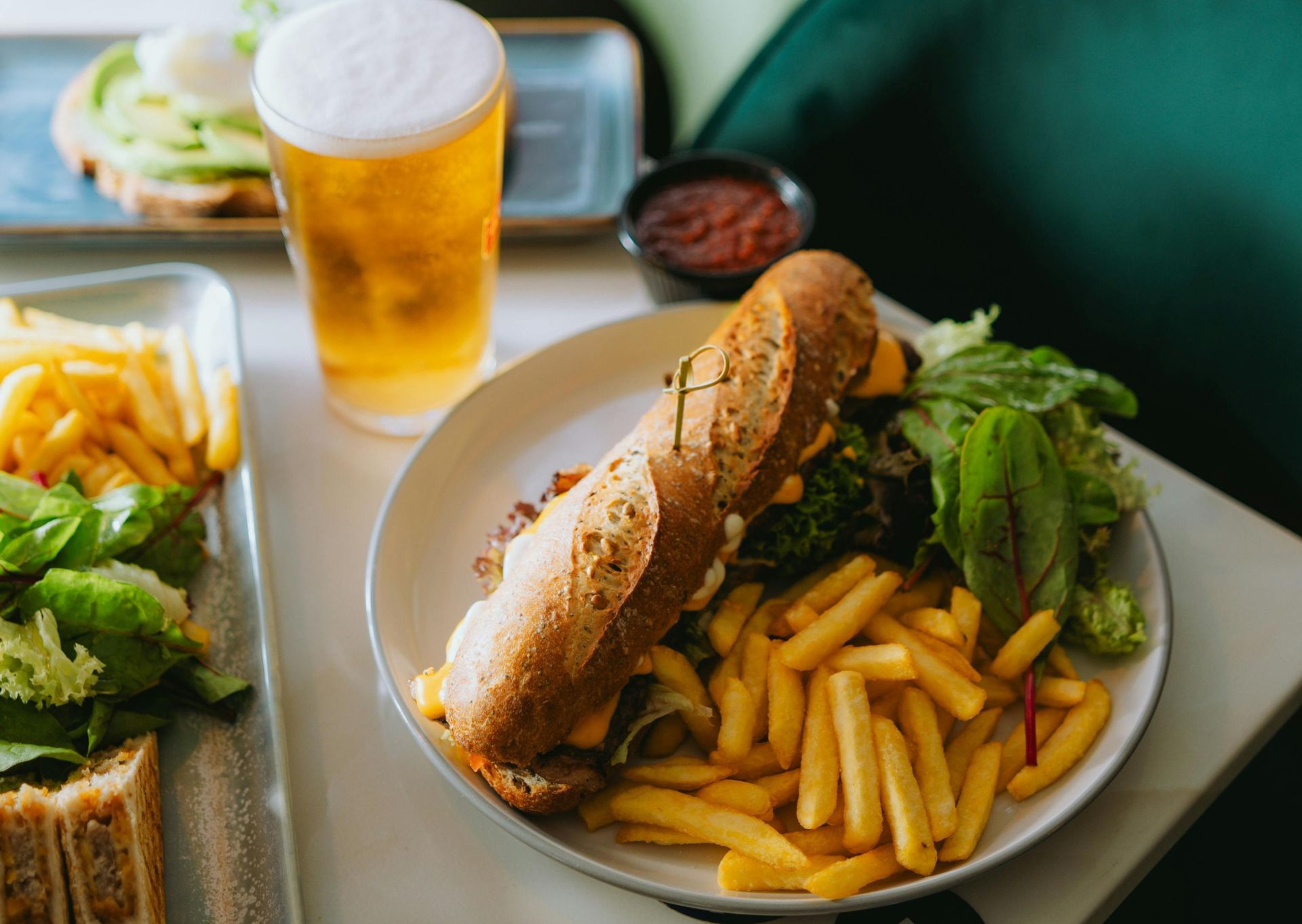 Plate with sandwich, fries, and beer in a cozy cafe setting.