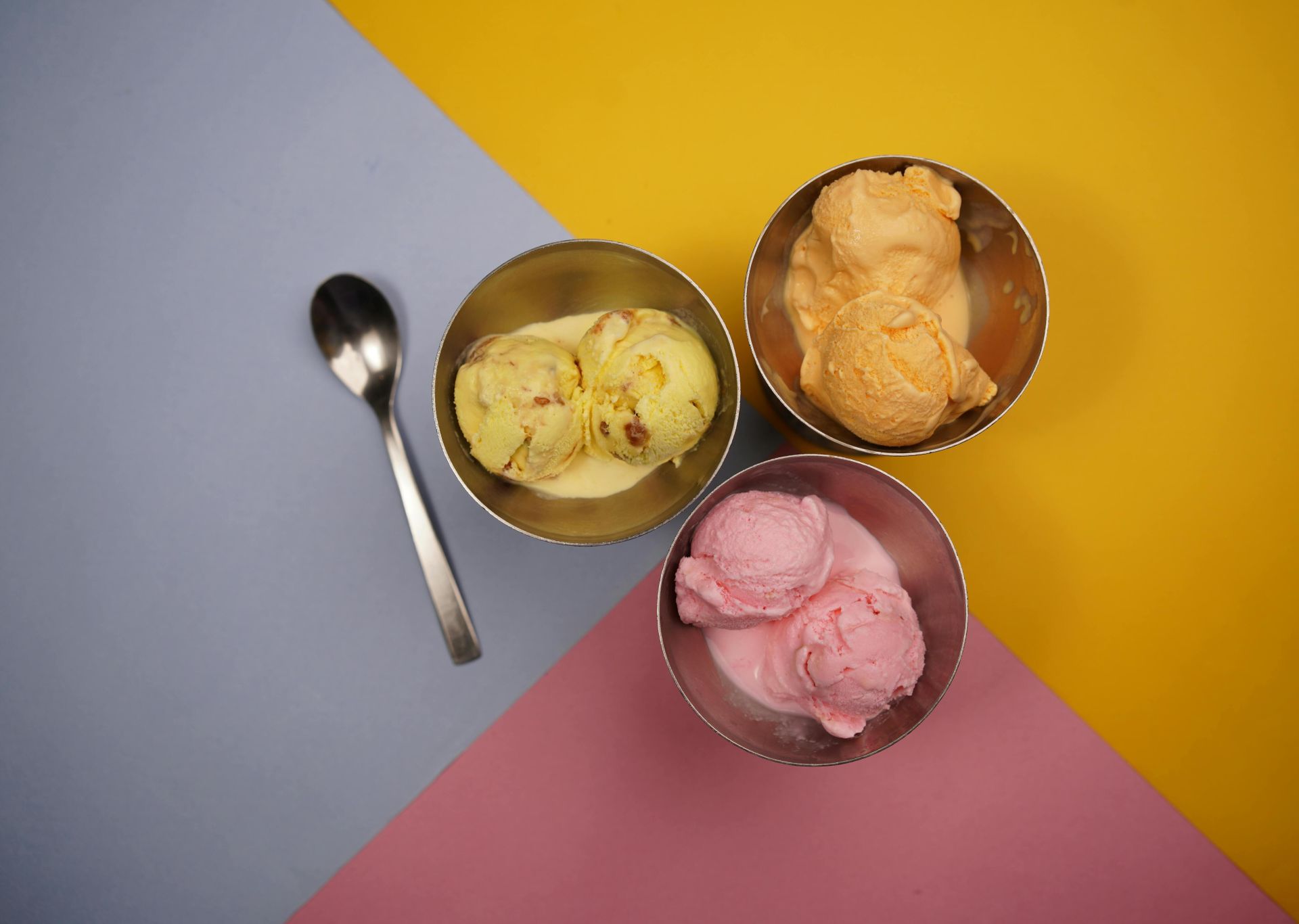 Vibrant ice cream scoops in metal bowls on colorful background.