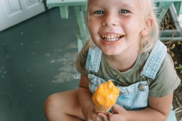A happy child enjoying a delicious ice cream cone, sitting indoors on a summer day.