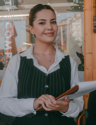 Smiling waitress holding menu at a cozy restaurant in Kütahya, Türkiye.